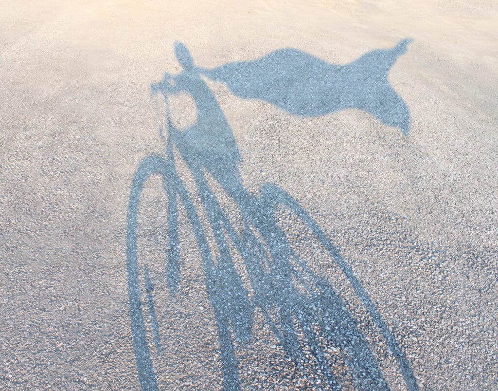 kid shadow riding bike with superhero cape
