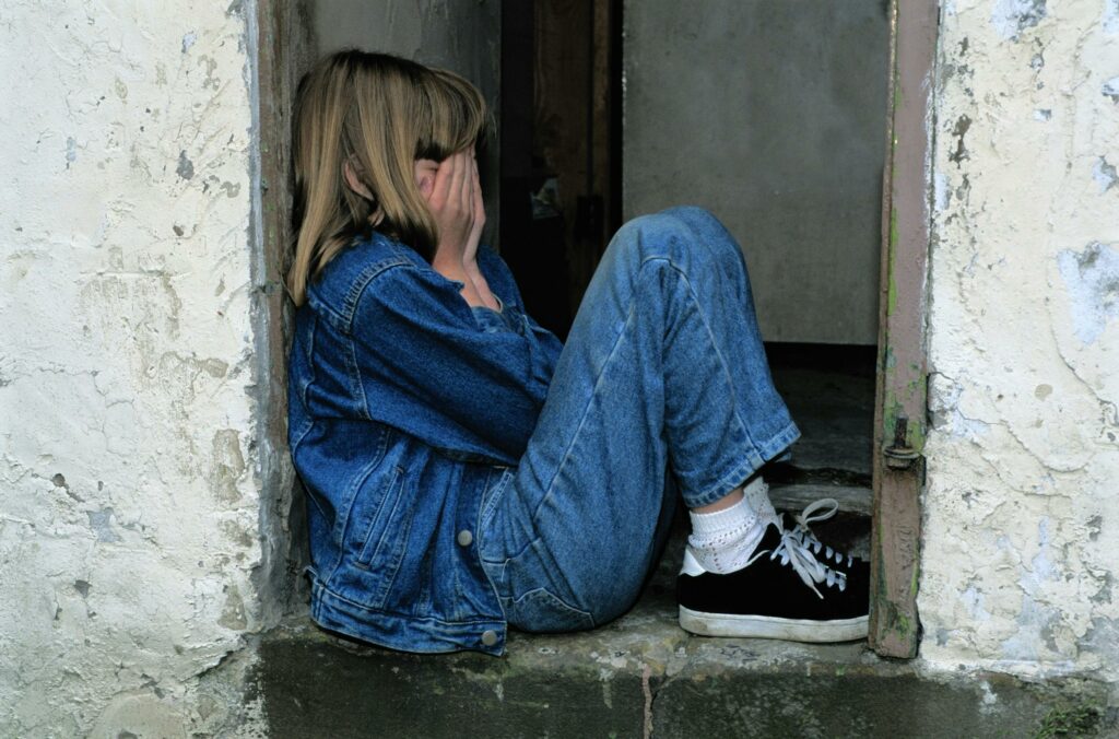 a child sitting in a corner, upset, wearing denim