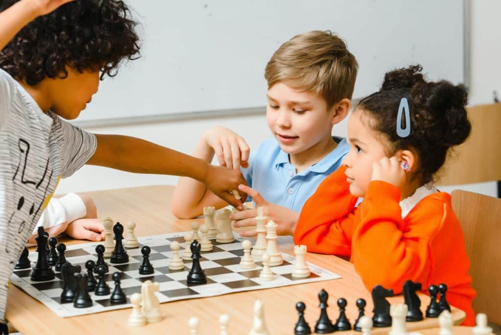 three kids playing chess in a classroom