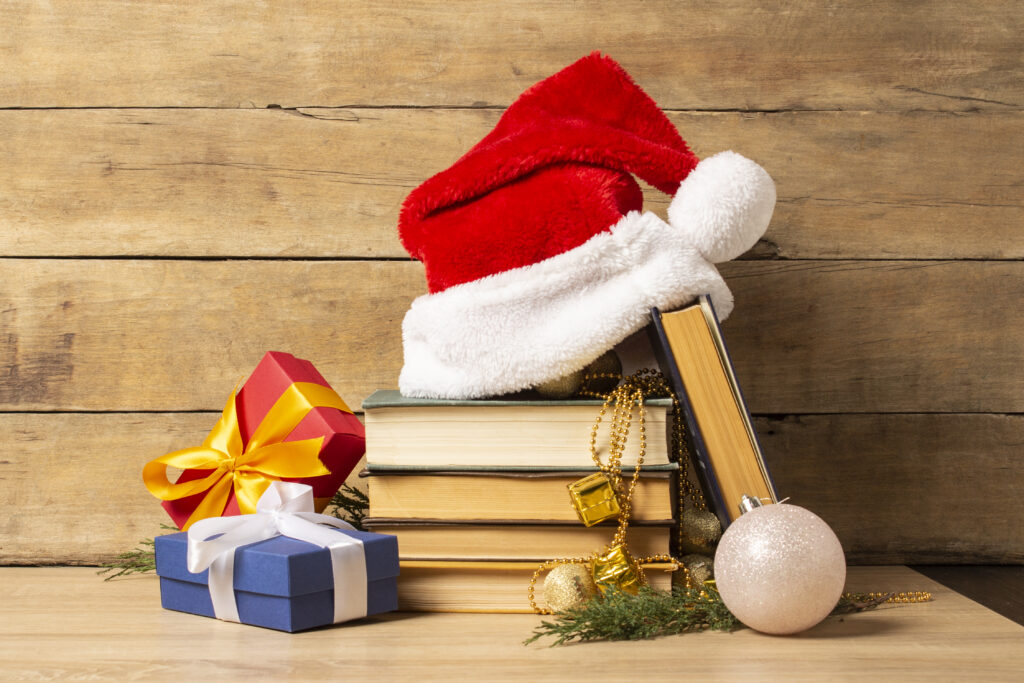 Pile of books, Santa Claus hat, Christmas-tree decorations and Gifts on a wooden background.